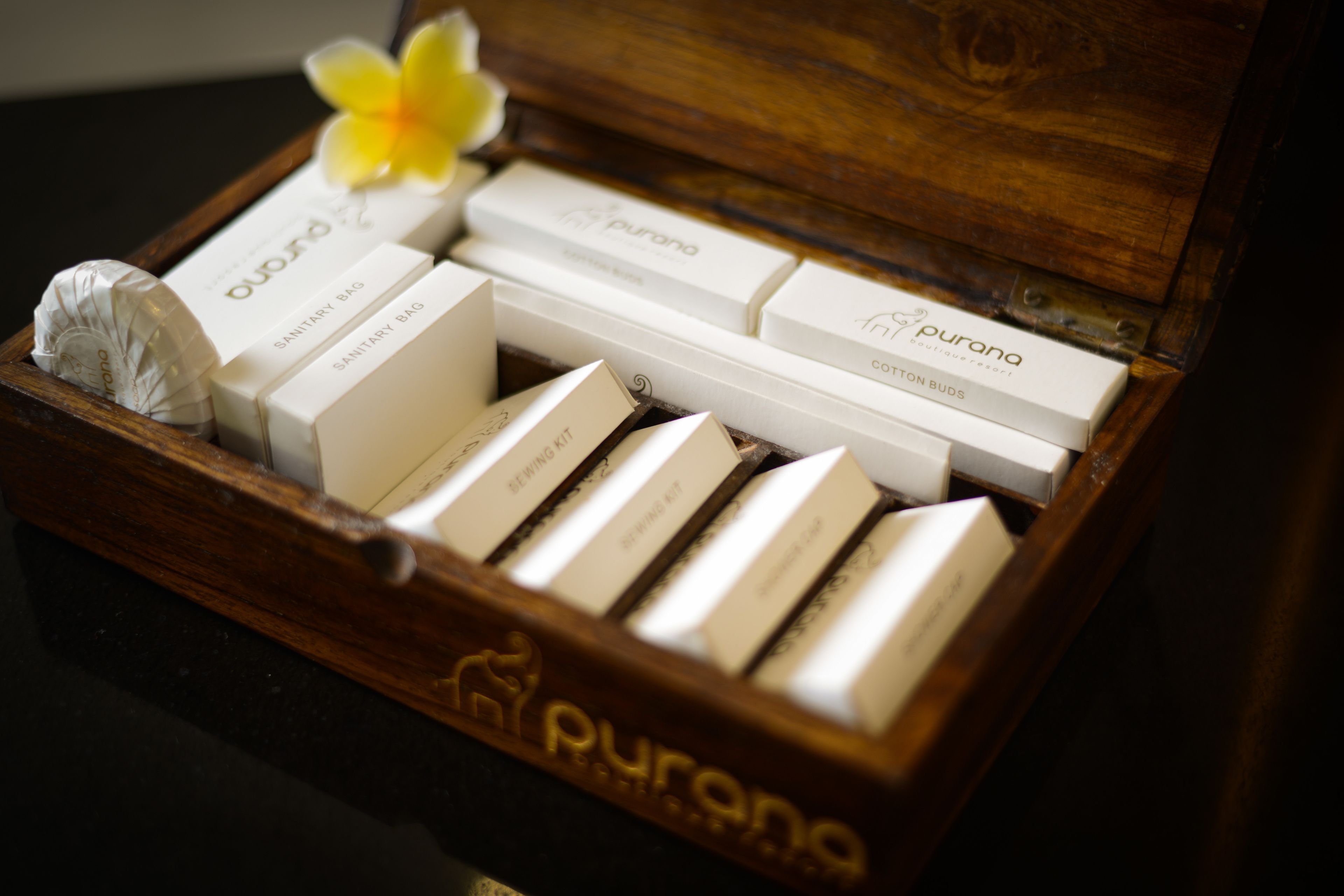 A wooden box containing various items including a sewing kit, cotton buds, and a sanitary bag.