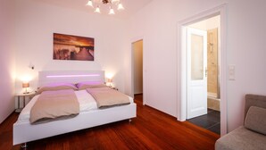 Quarto moderno com uma cama grande, luminárias laterais, uma obra de arte na parede e piso de madeira.