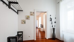 Um corredor com piso de madeira, um banco preto, um vaso e uma porta que dá para outro cômodo.
