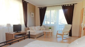 A hotel room with a bed, a sofa, a TV, a chair, and a balcony with curtains. - Pension AdlerHorst (Steindorf am Ossiacher See)