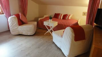 A cozy room with two white armchairs, a red and white checkered bed, and a small white table with a plant.