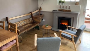 A cozy living room with a wooden bench, a fireplace, a television, and a window with plants. - Pension AdlerHorst (Steindorf am Ossiacher See)