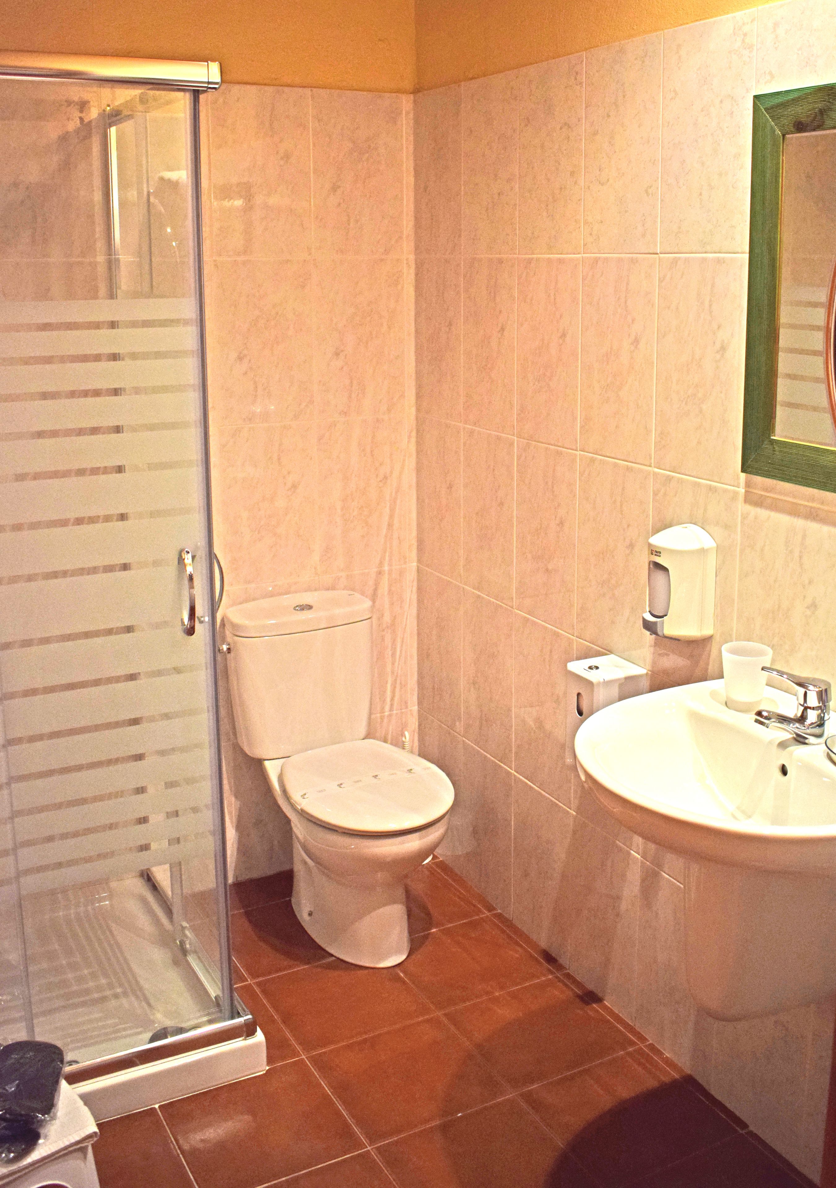 Un baño con cabina de ducha de vidrio, un inodoro y un lavabo con dispensador de jabón.
