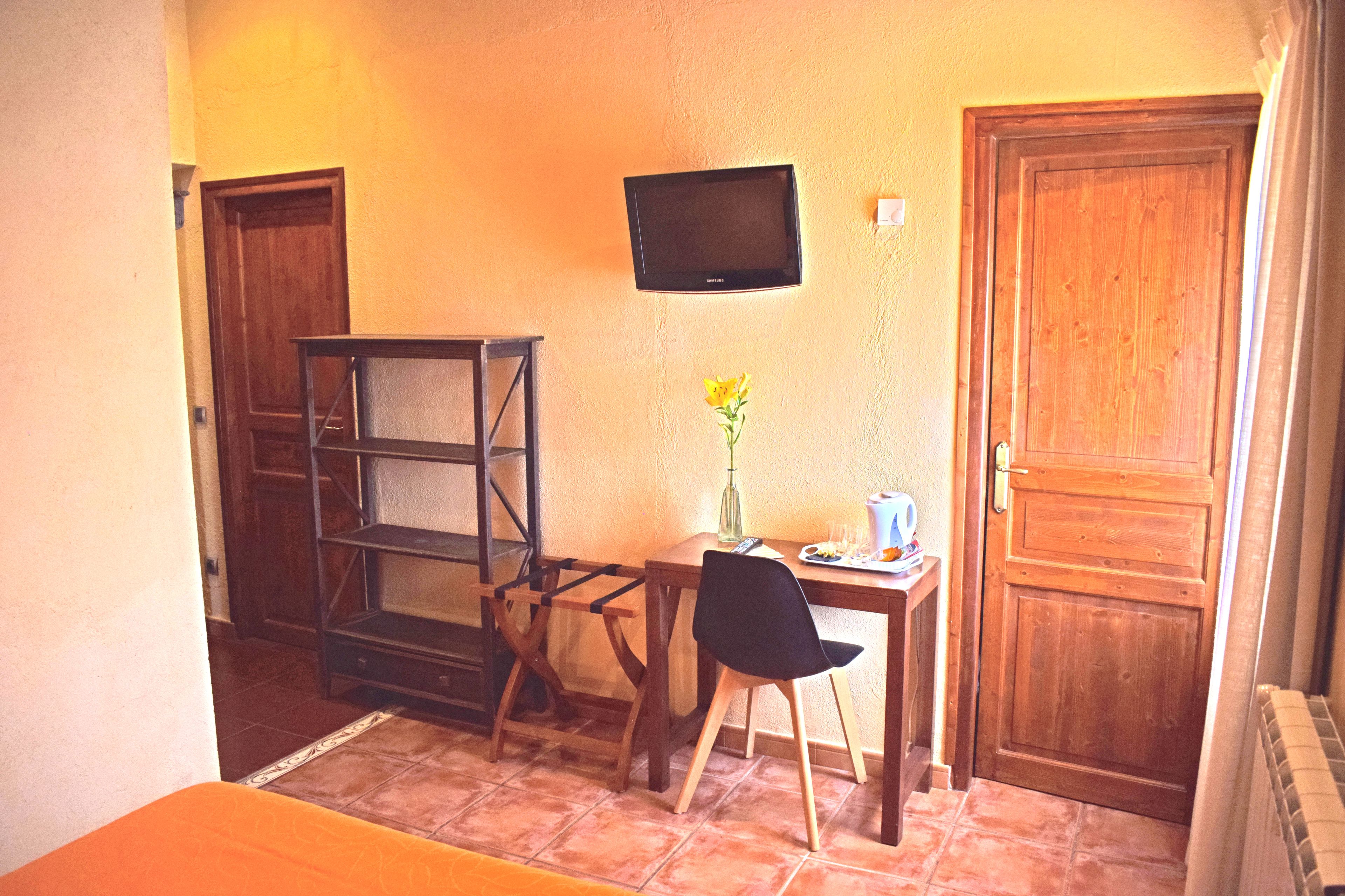 A small room with a wooden desk, a chair, a television mounted on the wall, and a door.