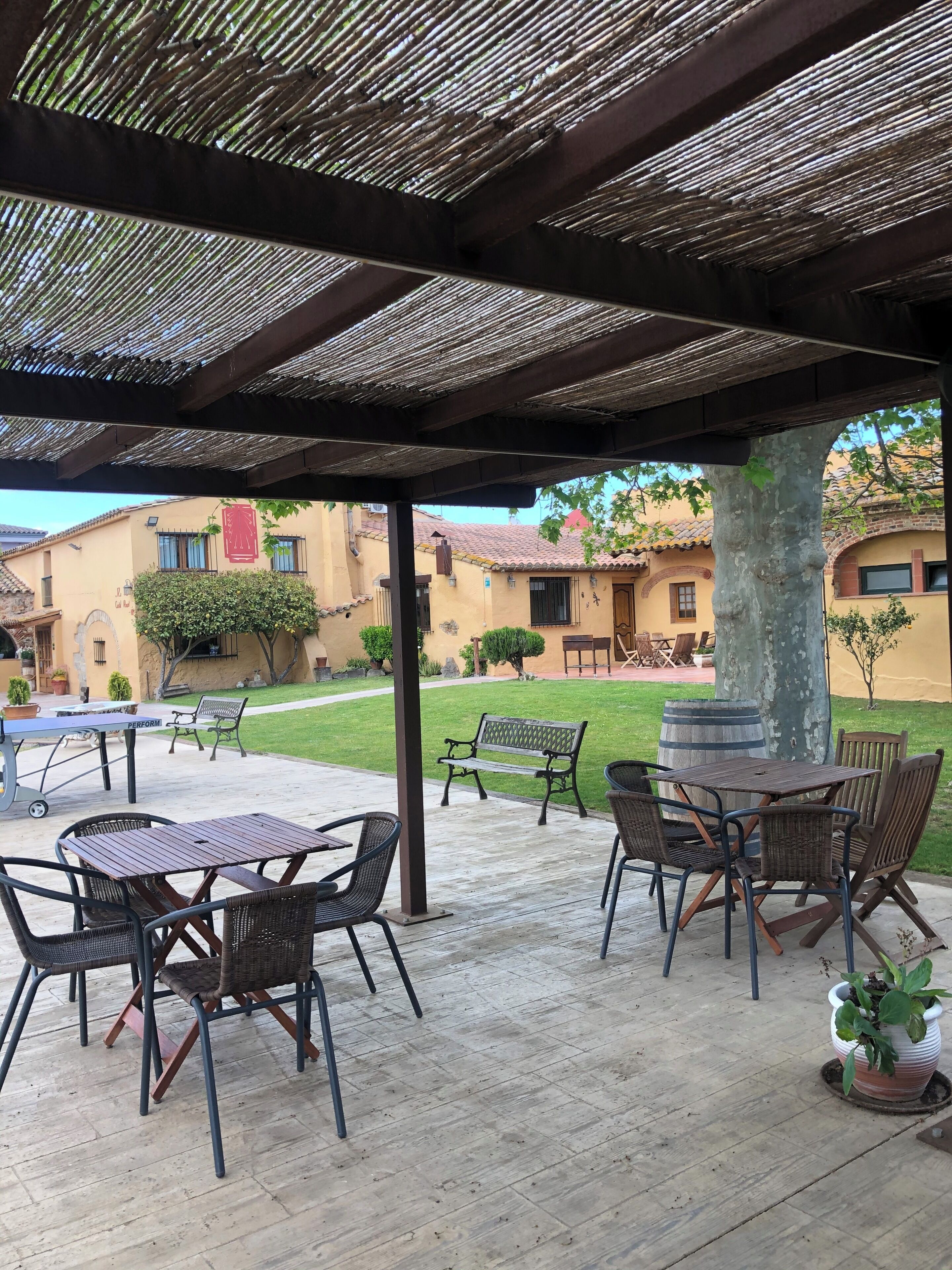 Eine Außenpatio mit Tischen und Stühlen, einer darüberliegenden Pergola und Blick auf Gebäude im Hintergrund.