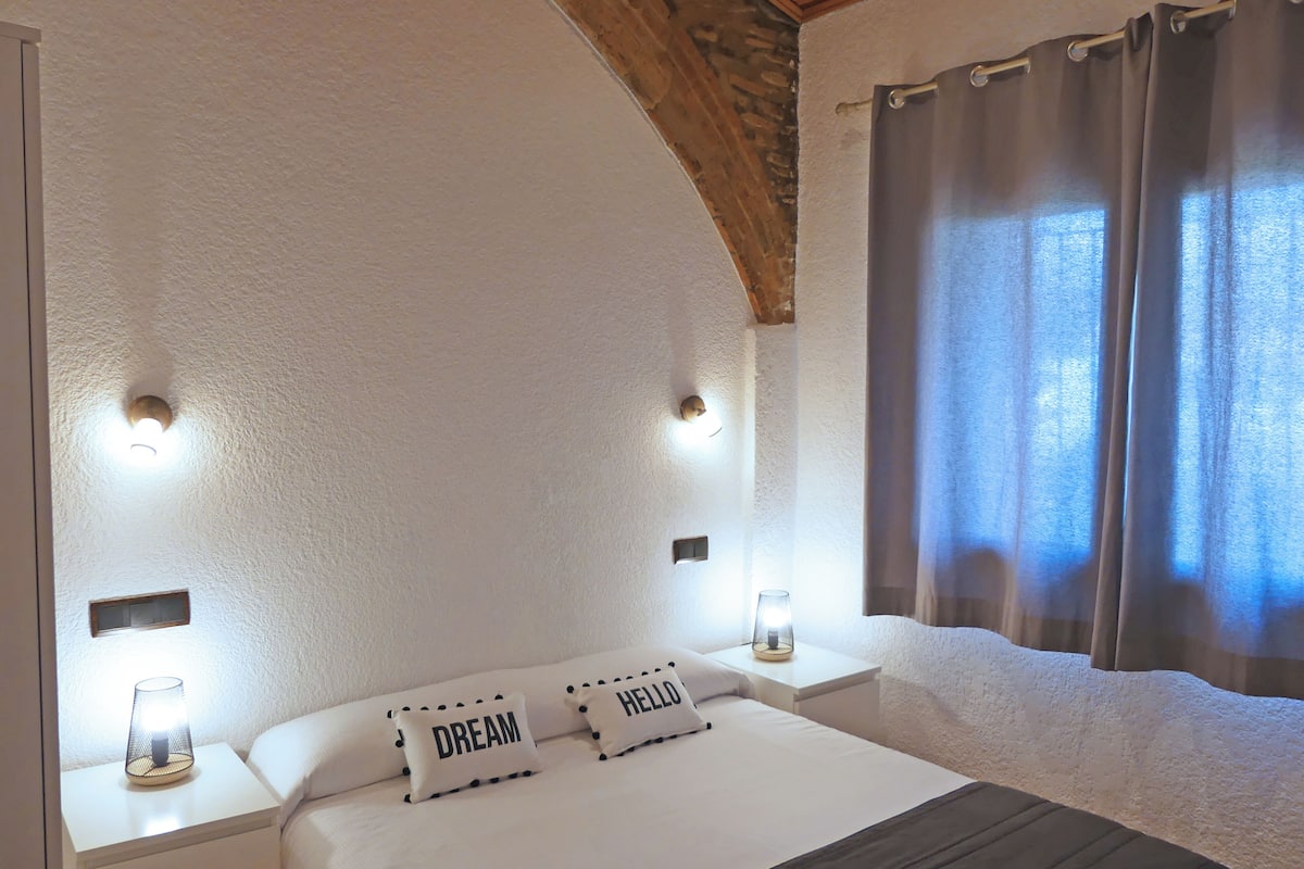 A bedroom with a white bed, two bedside lamps, and a window with curtains.