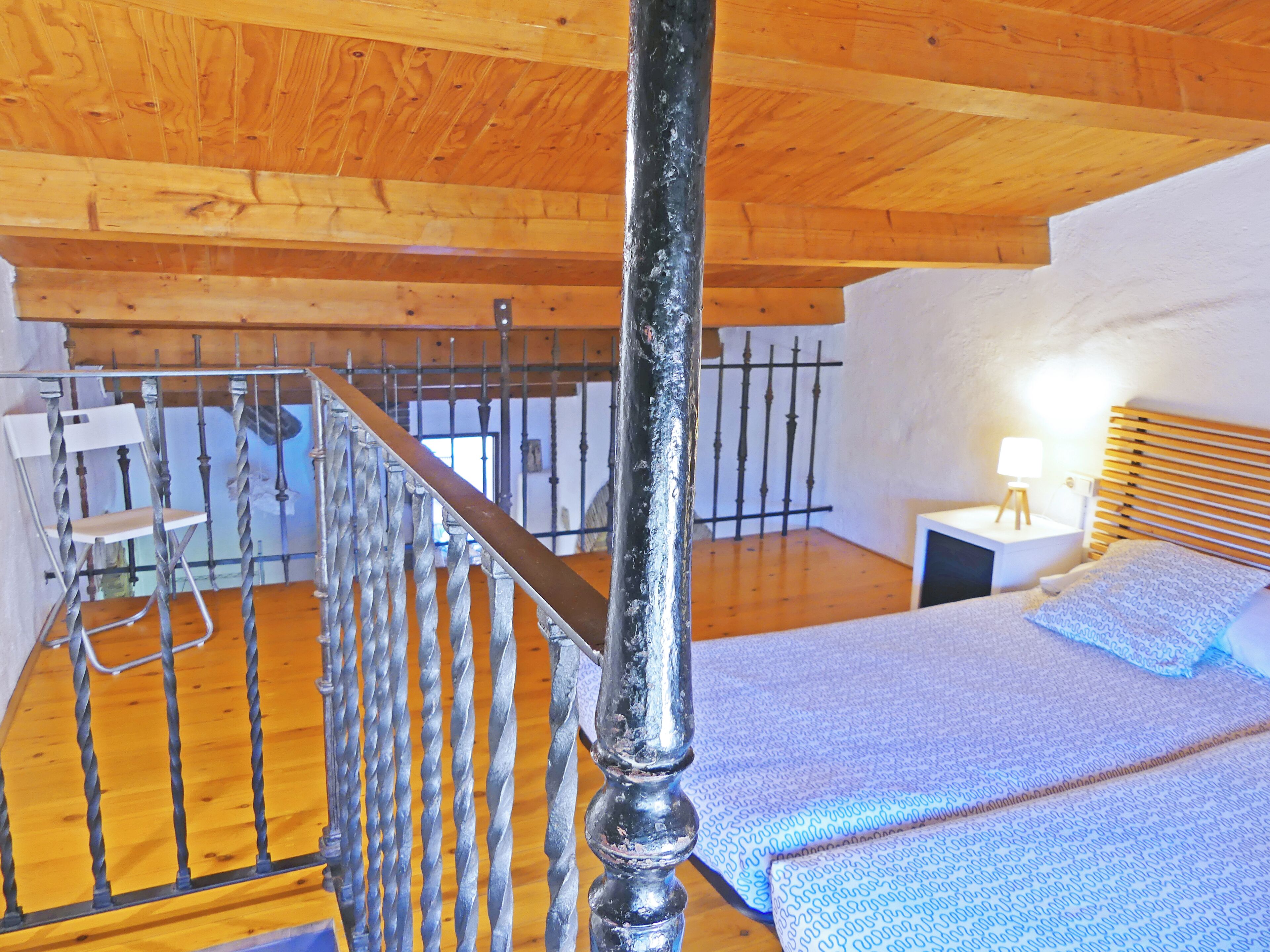 Una escalera de madera con barandales de metal que lleva a un dormitorio con una cama y una mesita de noche.