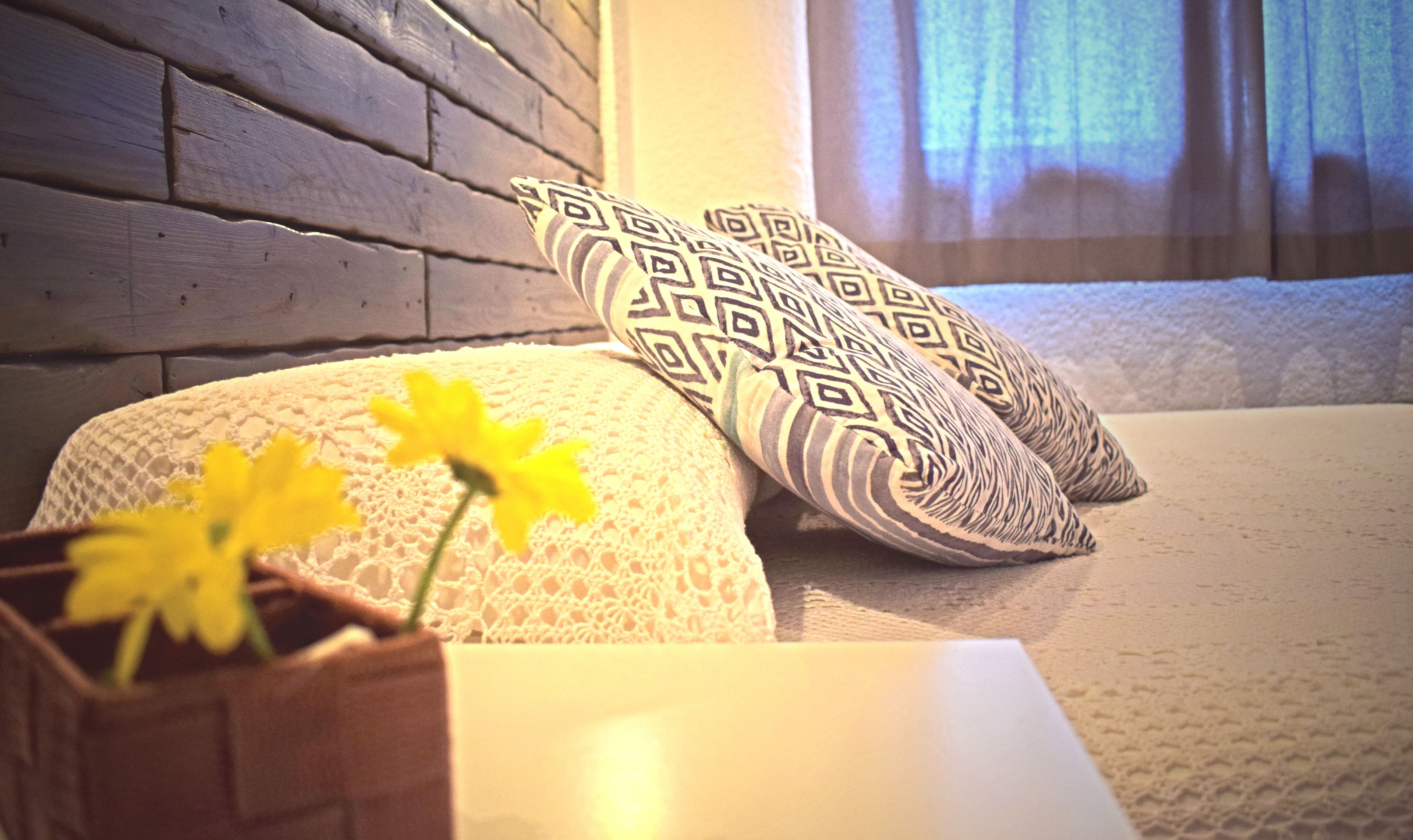 A bed with patterned pillows, a vase with flowers, and a wooden wall.