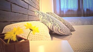A bed with patterned pillows, a vase with flowers, and a wooden wall.