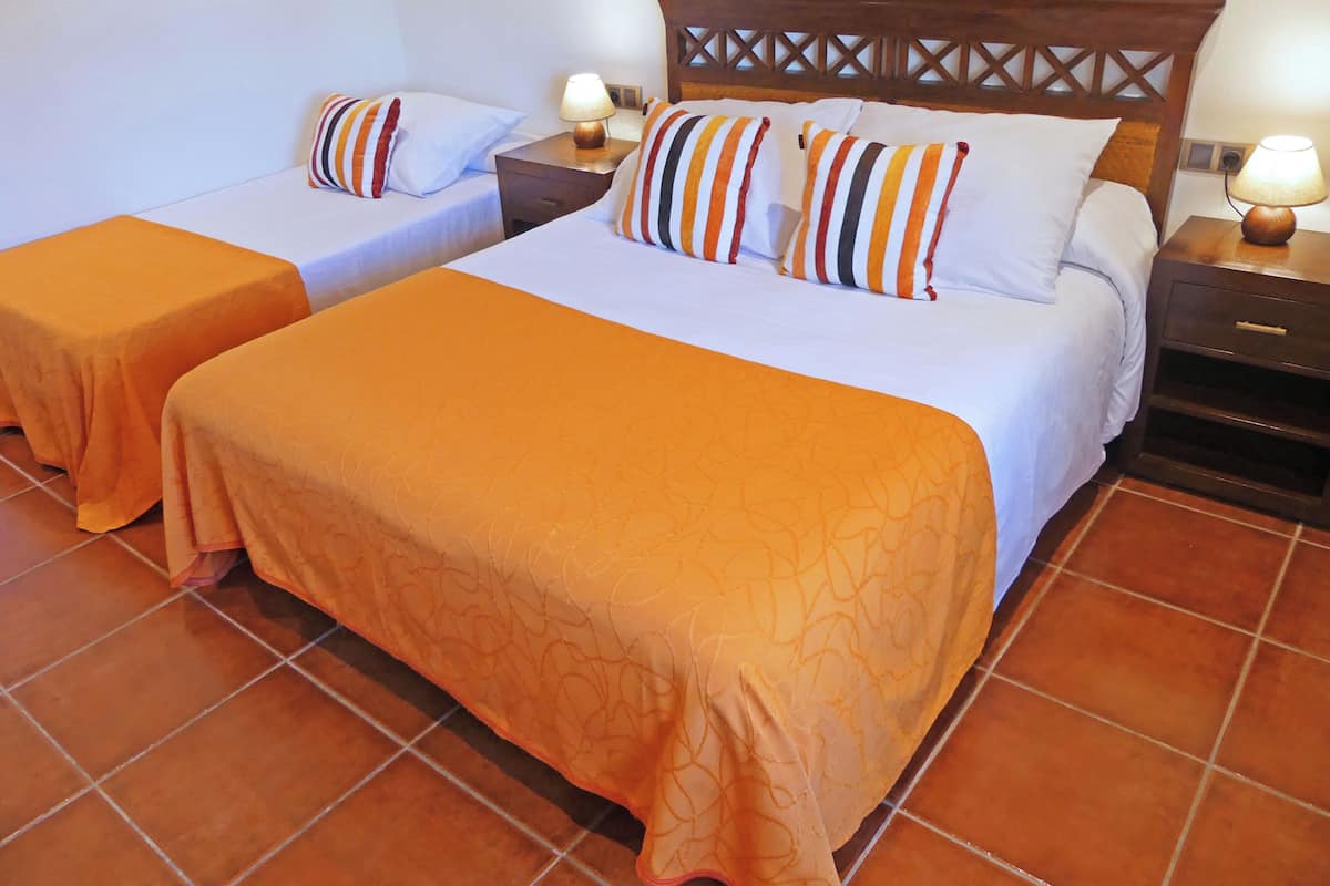 A hotel room with two beds, each with an orange bedspread and striped pillows. There are wooden nightstands with lamps and a wooden headboard with a lattice design.
