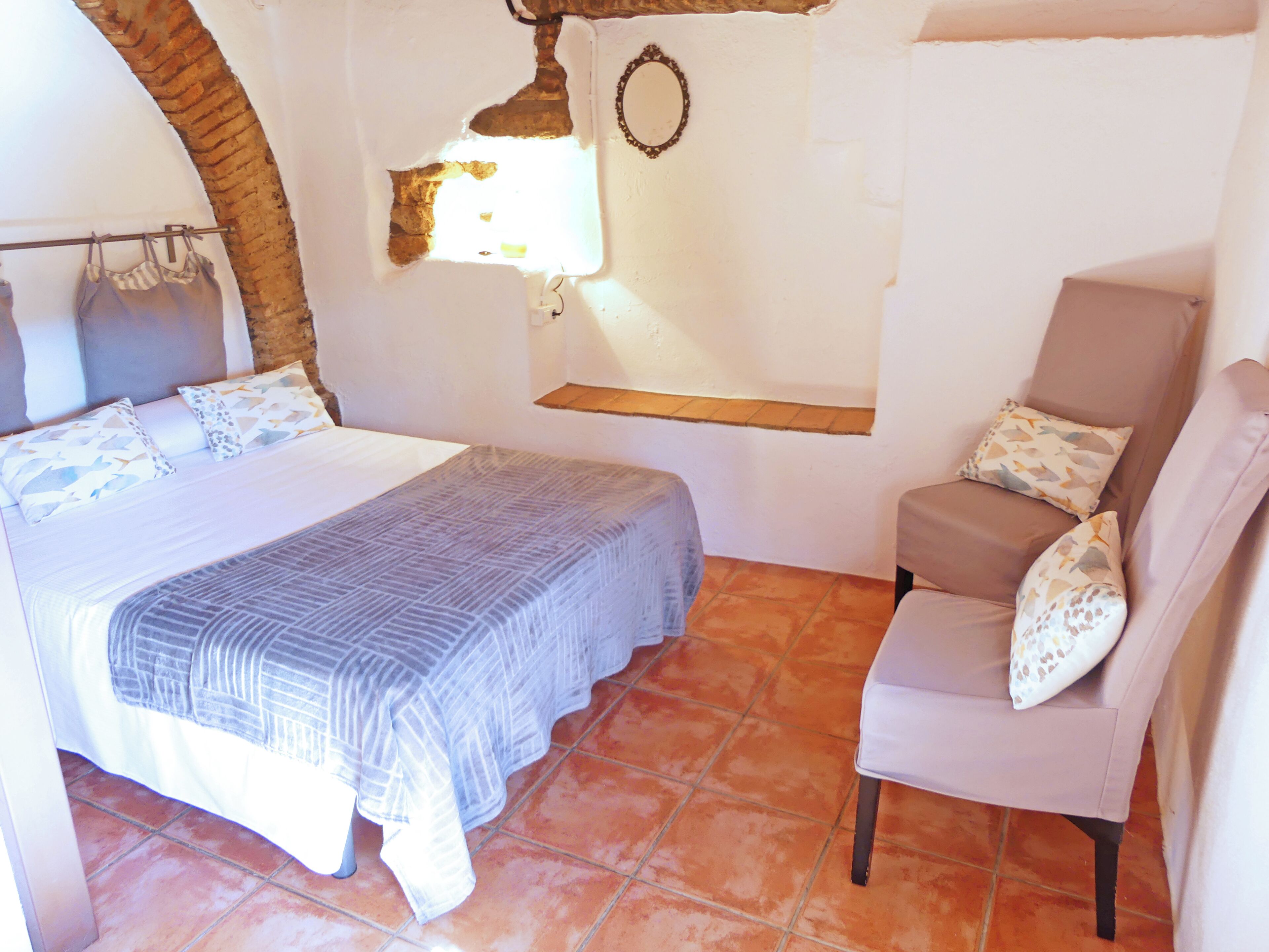 A bedroom with a bed, a chair, a small table, and a window.