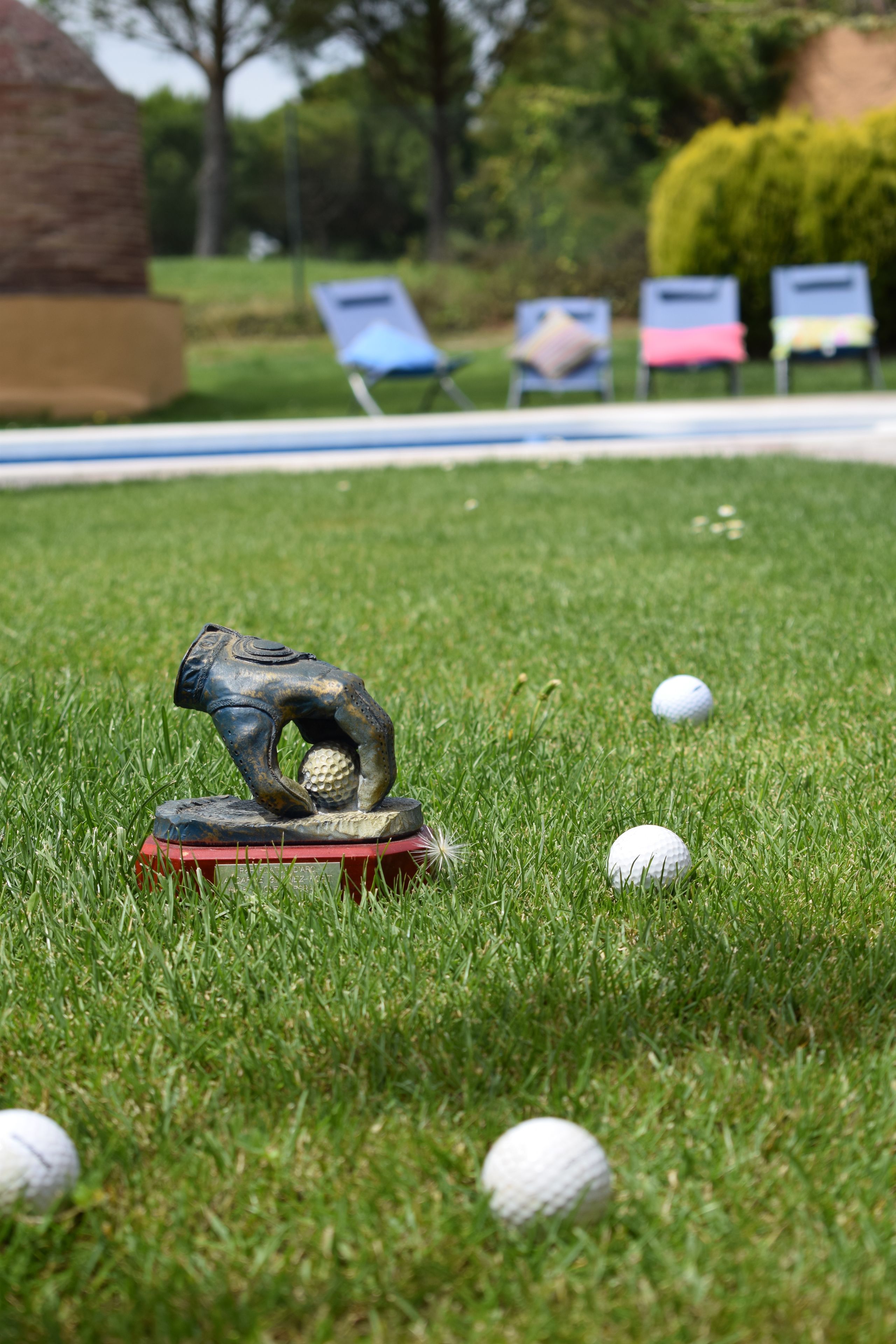 Un campo da golf con una scultura di un golfista su una base rossa, diverse palline da golf e sedie a sdraio sullo sfondo.