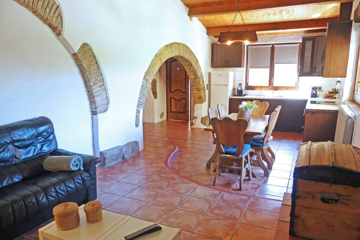 A living room with a leather sofa, a dining table with chairs, a kitchen area, and a fireplace.