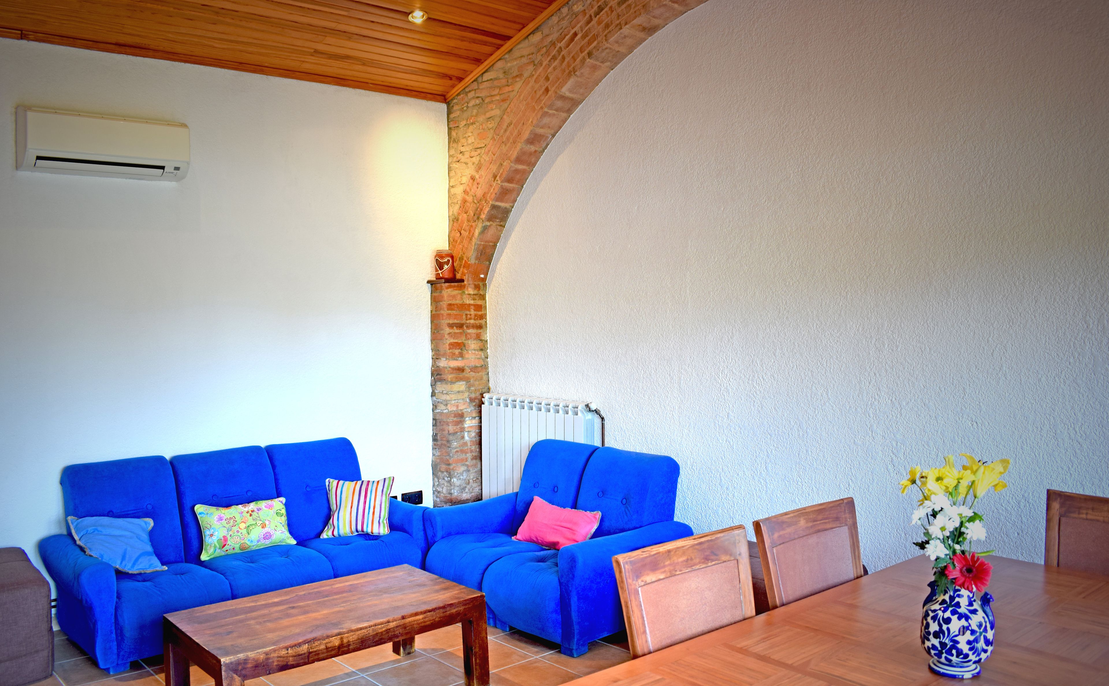 Una habitación con un sofá azul, una mesa de centro de madera, una mesa de comedor con sillas y un jarrón con flores.