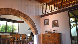 Un comedor con sillas de madera y una mesa, un arco de piedra, un armario de madera y un balcón con barandilla.