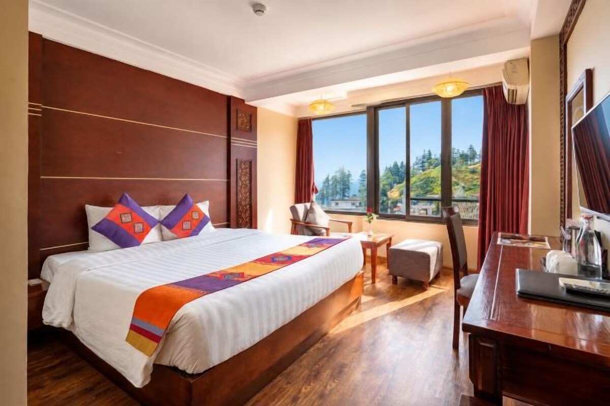 Ein Hotelzimmer mit einem großen Bett, einem Schreibtisch, einem Stuhl und Blick ins Freie.