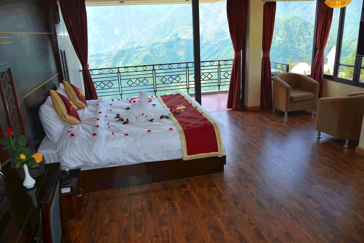 Een slaapkamer met een groot bed, een balkon met uitzicht op de bergen en een stoel.