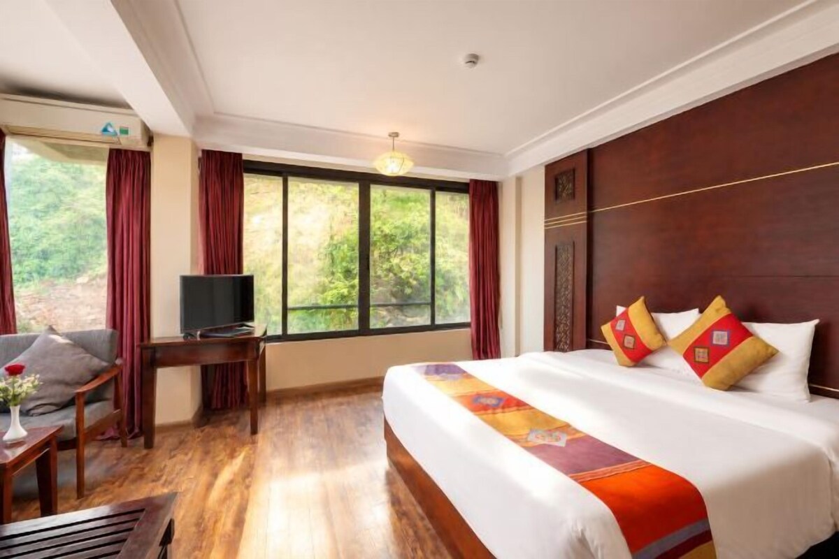 Ein Hotelzimmer mit einem großen Bett, einem Fernseher, einem Schreibtisch und Blick ins Freie.