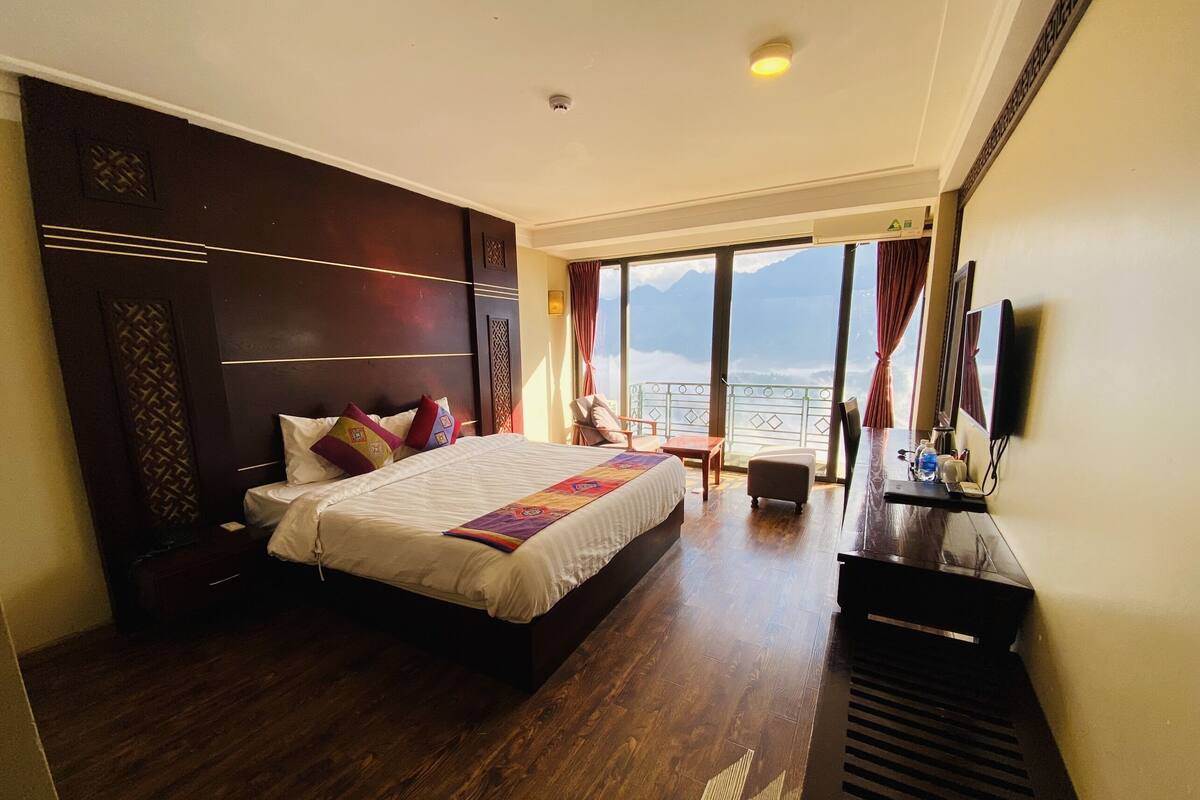 Een hotelkamer met een groot bed, een bureau met stoel, een televisie en uitzicht op zee.