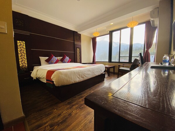 A hotel room with a large bed, a wooden desk, and a view of mountains through the window. - Sapa Vista Hotel (Sa Pa)