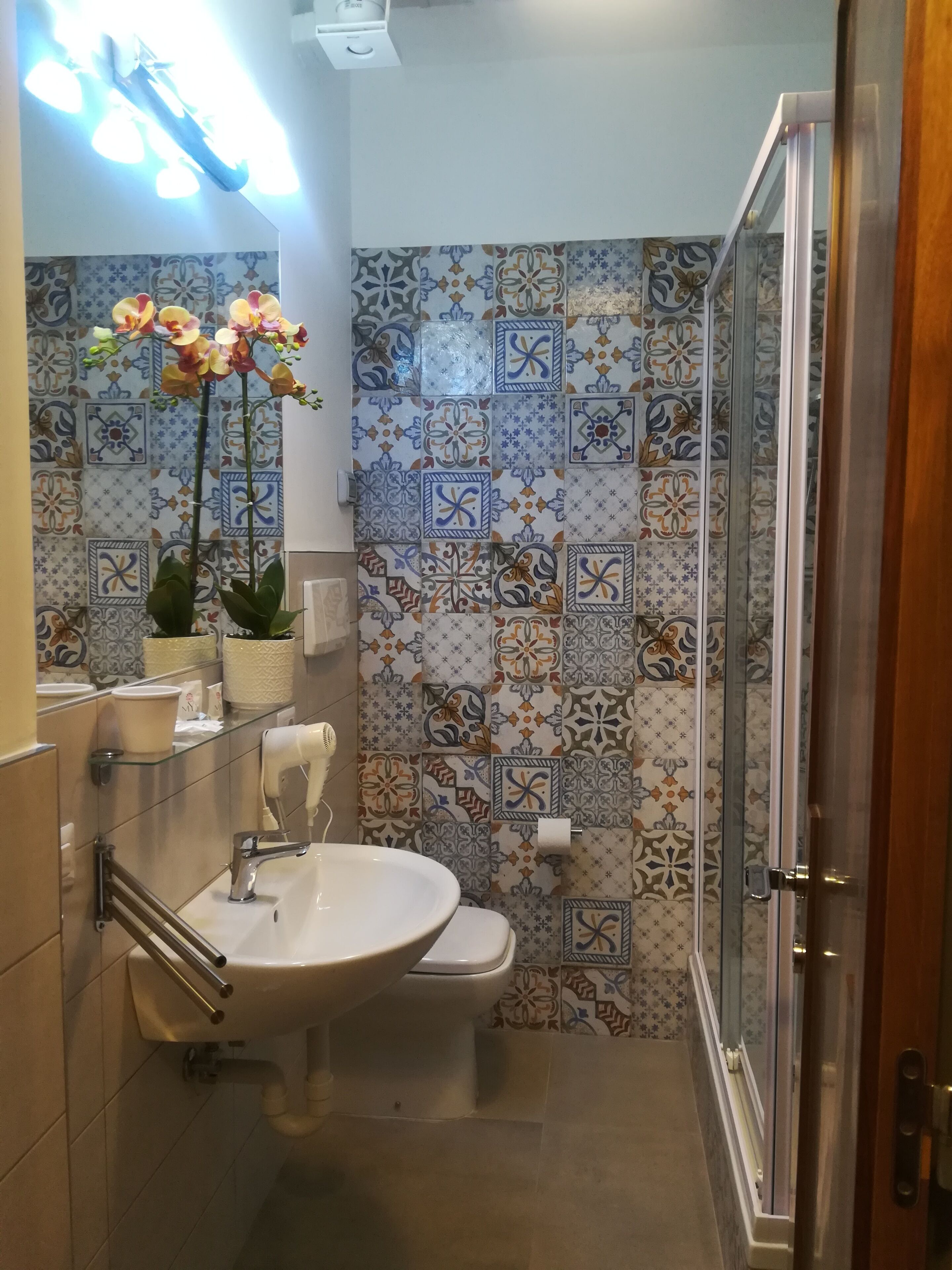 Une salle de bain avec un lavabo, des toilettes et une douche. Les murs sont décorés de carreaux à motifs.