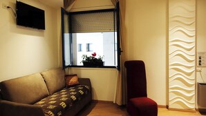 A living room with a sofa, a red chair, a window with a view, a flat-screen TV, and a wall-mounted radiator. - Piazza Mulino 26 (Matera)