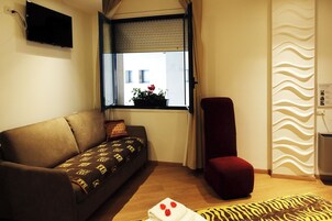 Un soggiorno con divano, una poltrona rossa, una finestra vista, televisione a schermo piatto e termosifone a parete.