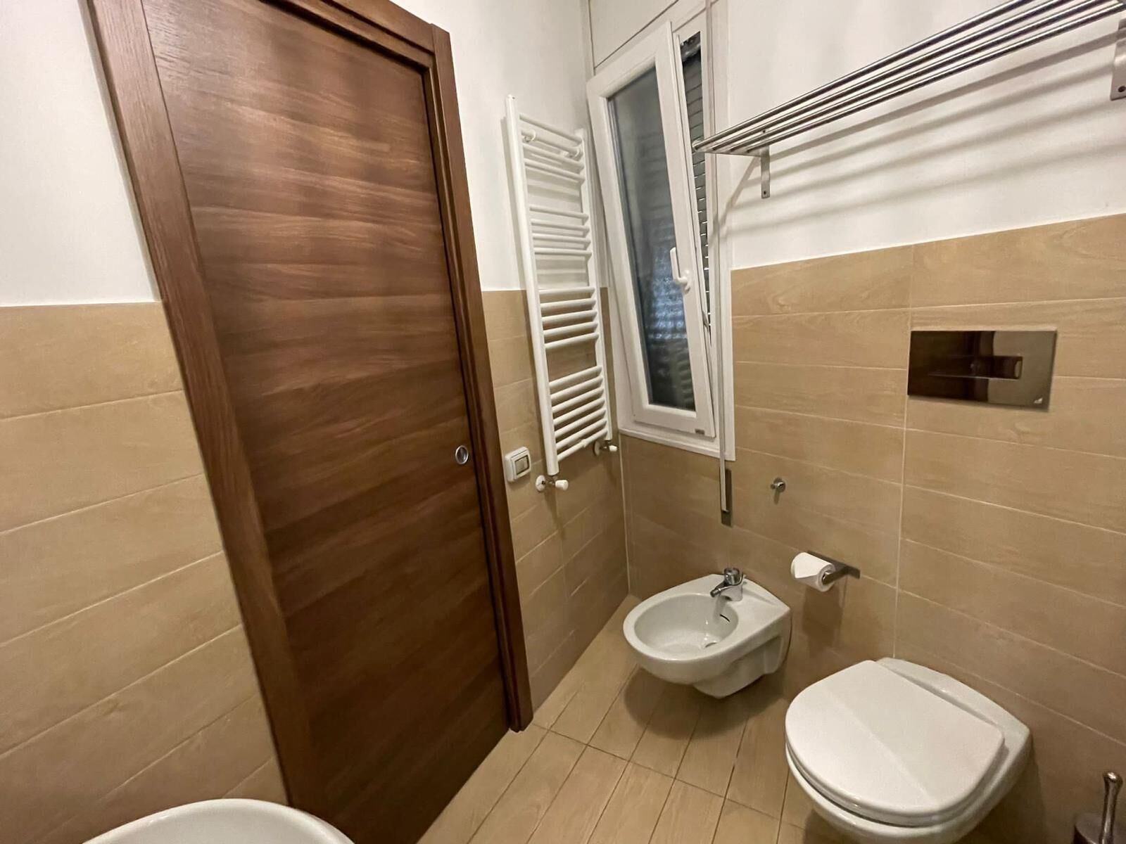 A bathroom with a wooden door, a bidet, a toilet, and a towel rack.