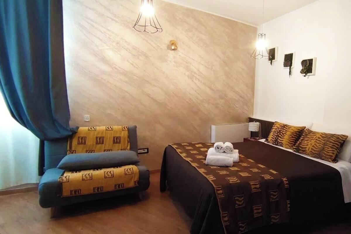 Una habitación de hotel con cama, sofá, escritorio e iluminación fijada a la pared.