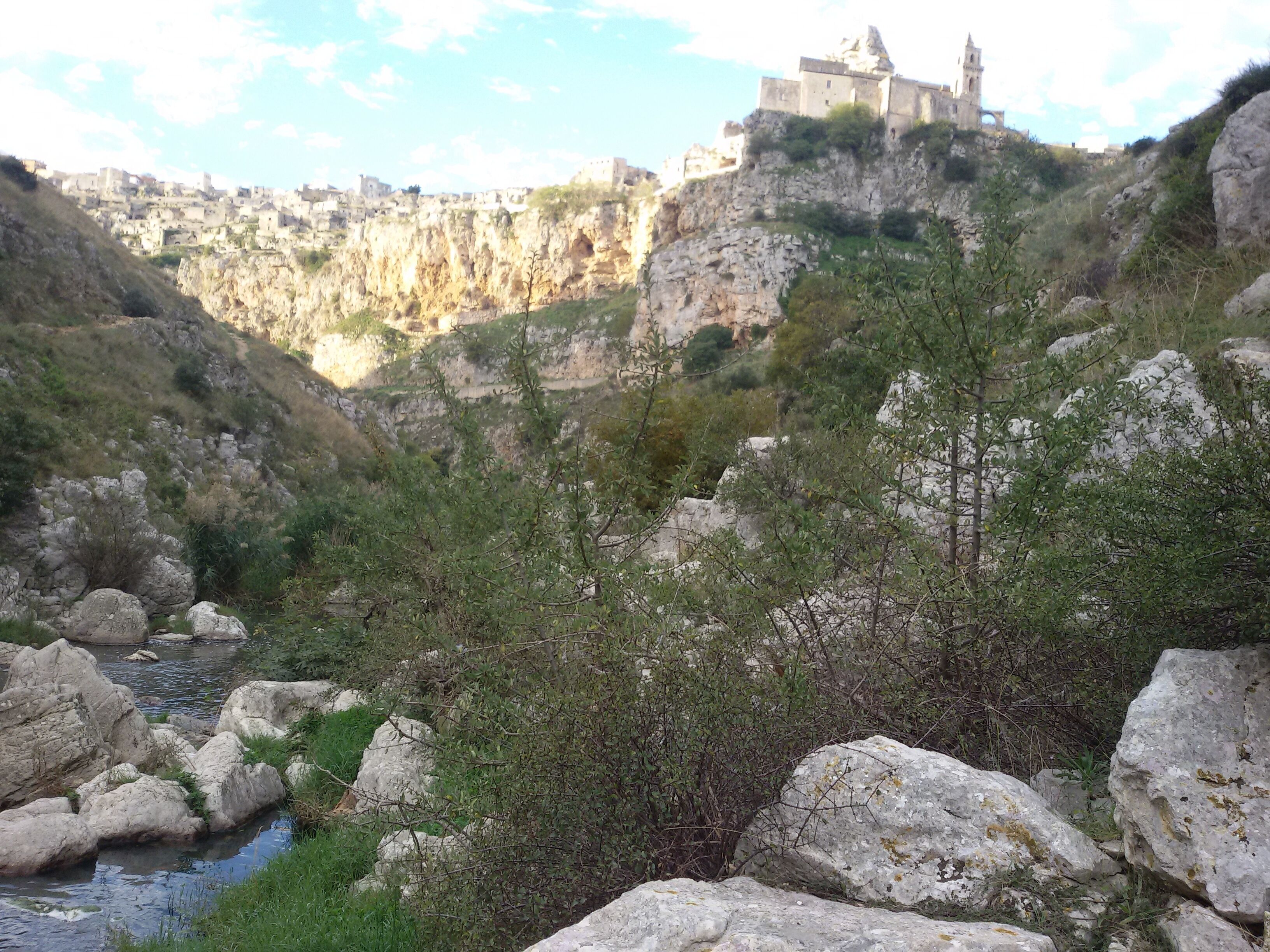 Un paisaje rocoso con un río, vegetación densa y un edificio histórico en un acantilado.