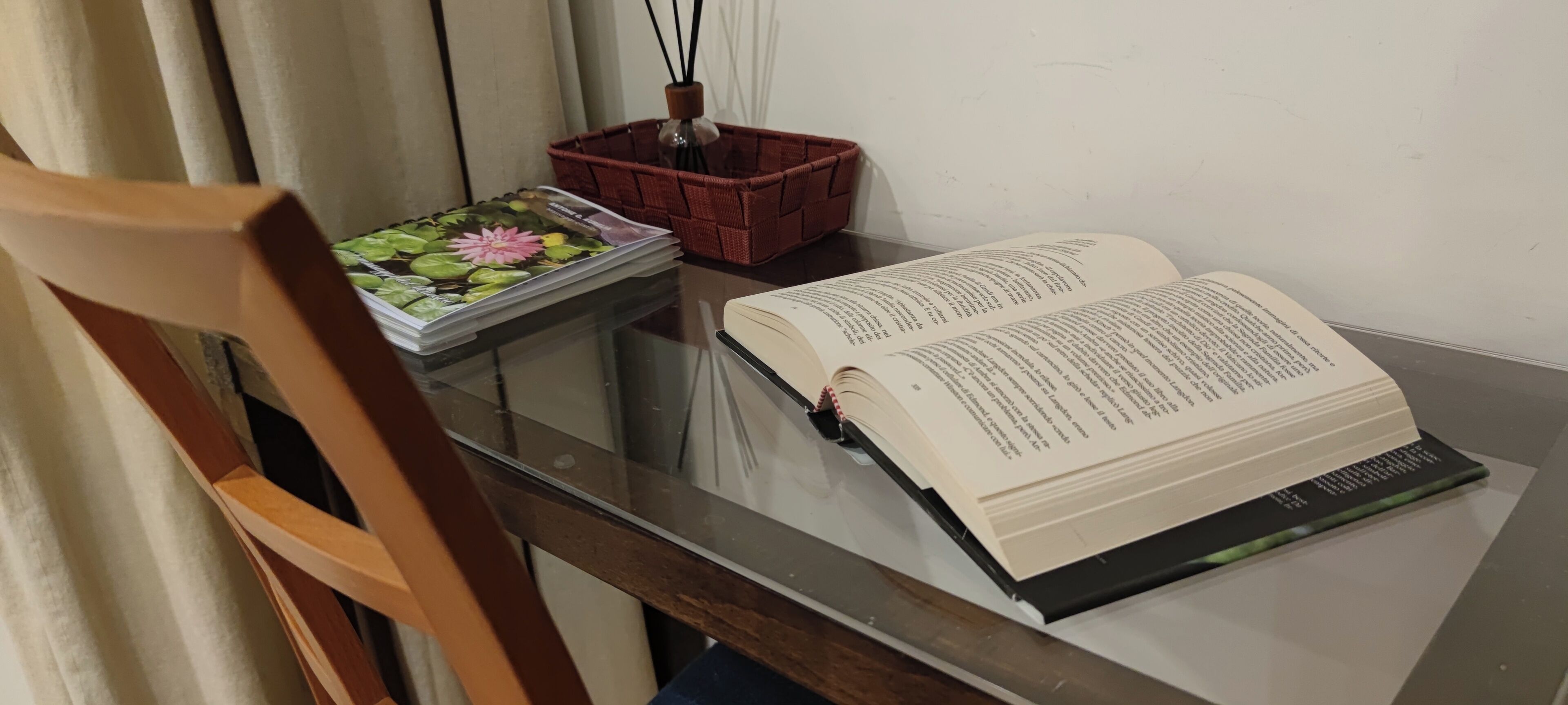 Un libro sobre una mesa de vidrio, una cesta roja y una silla de madera.