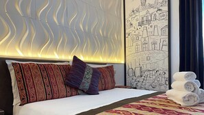 A hotel room with a neatly made bed, patterned pillows, a quilt, and a wall mural. - Piazza Mulino 26 (Matera)