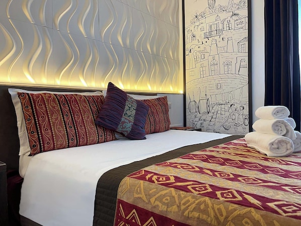 A hotel room with a neatly made bed, patterned pillows, a quilt, and a wall mural.