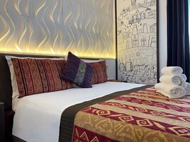 Una camera d'albergo con un letto rifatto, cuscini decorati, una coperta e un affresco sulla parete.