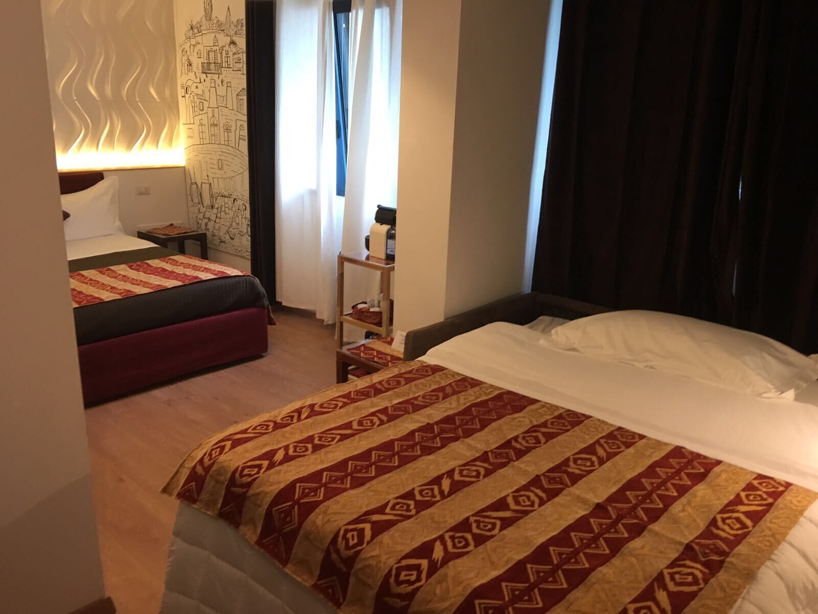 Habitación de hotel con dos camas, una mesita de noche, un mapa en la pared y una ventana con cortinas.