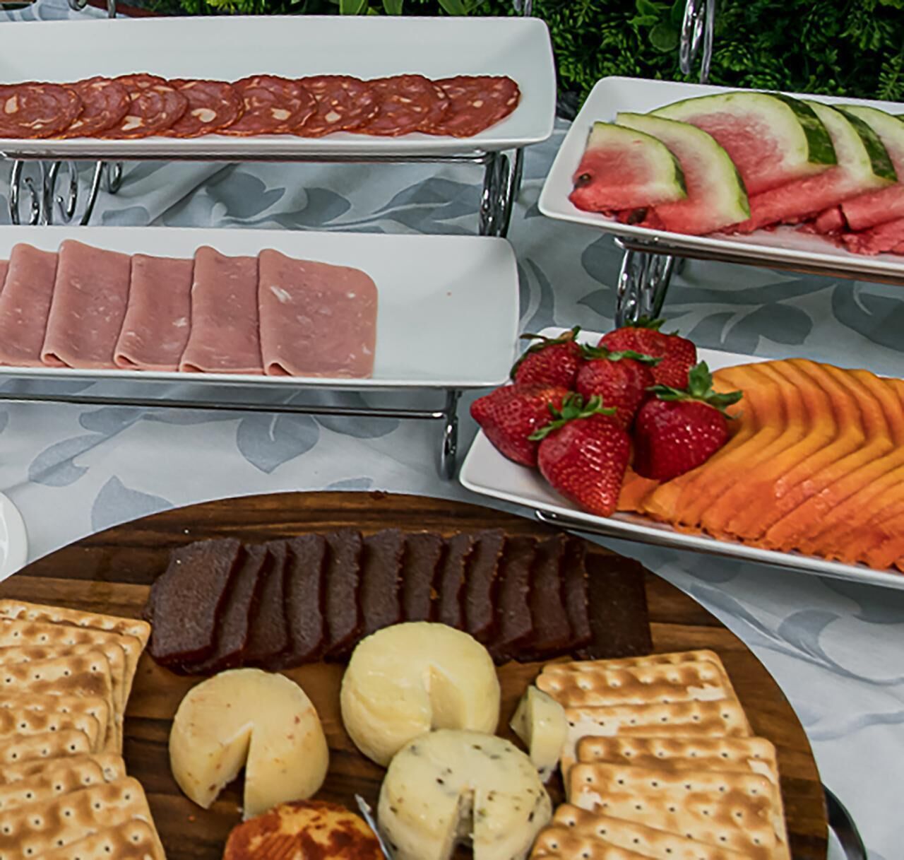 Un bufé con diversos alimentos, incluyendo carnes en rodajas, fresas, sandía y queso.