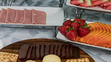 Un bufé con diversos alimentos, incluyendo carnes en rodajas, fresas, sandía y queso.