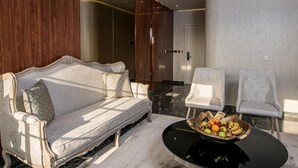 A modern living room with a white sofa, two armchairs, a black coffee table with fruit, and a unique chandelier. - Hotel Florença (Luanda)