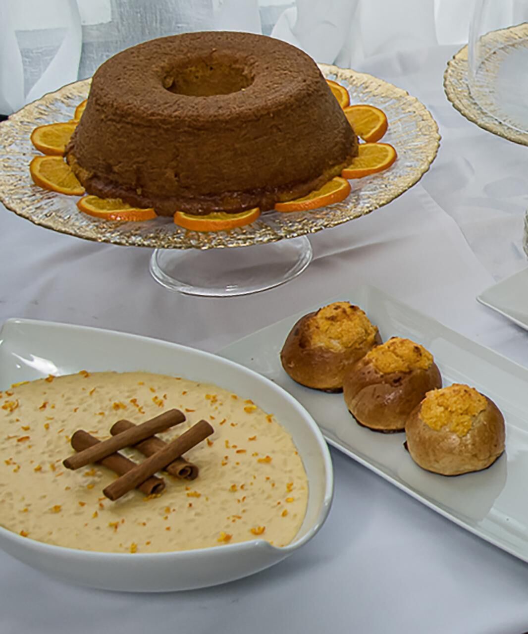 Una mesa de postres con un bizcocho bundt, un tazón de sopa adornado con canela en rama, y varios pastelitos.