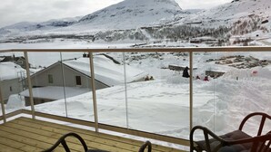 A wooden deck with two chairs, overlooking a snowy landscape with buildings and a mountain. - RIBO Apartment Riksgränsen (Riksgränsen)