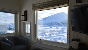 A living room with a large window offering a view of a snowy landscape and mountains. - RIBO Apartment Riksgränsen (Riksgränsen)