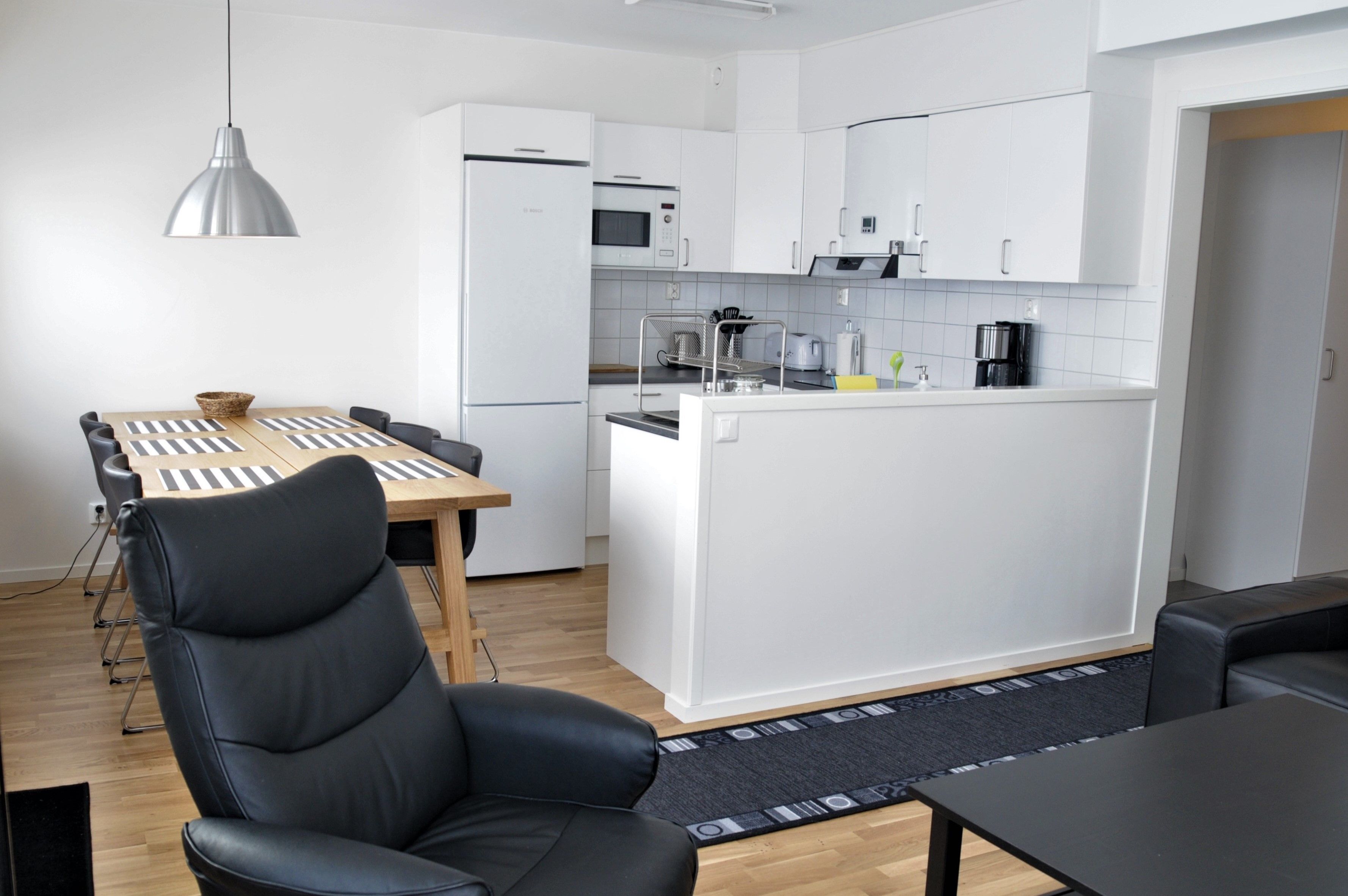 Una cocina moderna con armarios blancos, una isla central y un área de comedor con una silla negra y una mesa de madera.