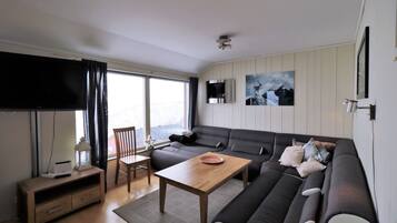 Ein modernes Wohnzimmer mit einer Couch, einem Holztisch, einem Fernseher und einem Essbereich mit Stuhl und Tisch.