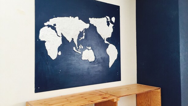 A world map on a dark wall with a wooden desk below. - The Evergreen Hostel (Hiroshima)