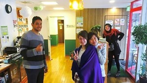 A hotel lobby with wooden flooring, a reception desk, and a glass partition with a view. - The Evergreen Hostel (Hiroshima)