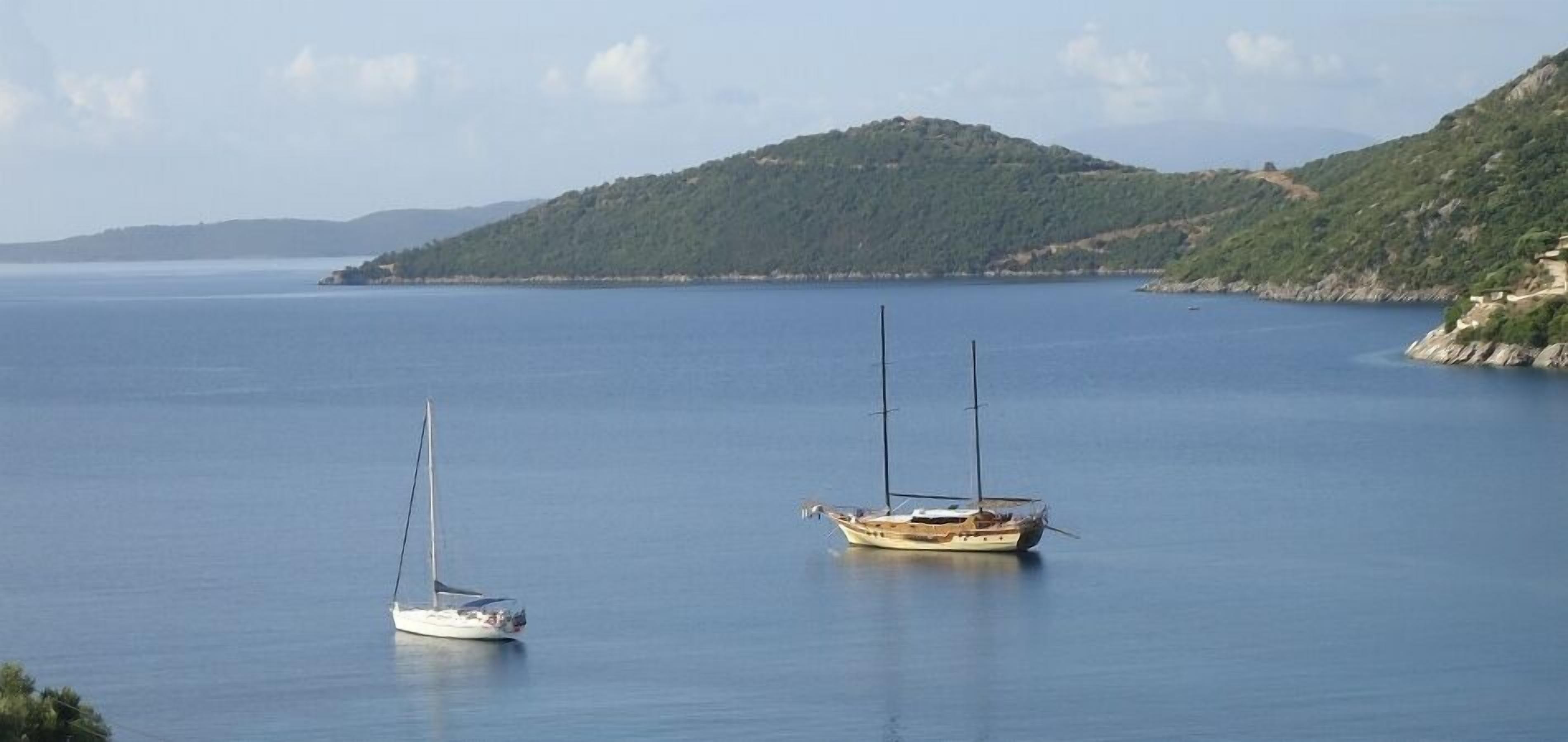 Mare calmo con due barche a vela ancorate vicino a una costa collinare.