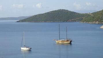 Mare calmo con due barche a vela ancorate vicino a una costa collinare.