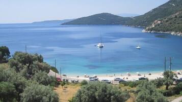 A coastal view with a beach, boats, and a hilly landscape.