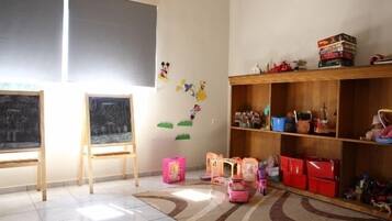 A classroom with two chalkboards, a wooden shelf with books and toys, and storage bins on the floor.