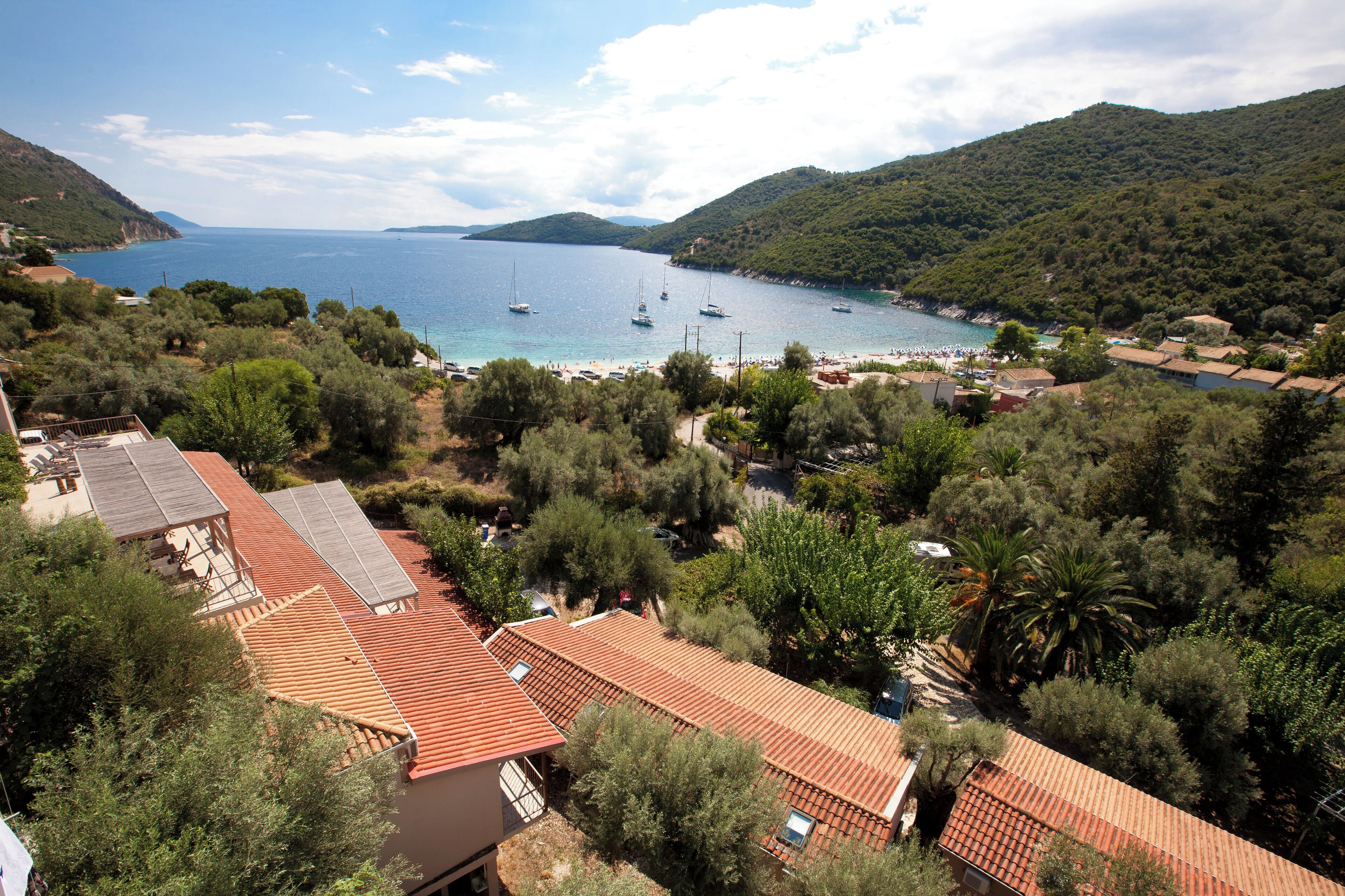 Un village côtier aux bâtiments aux toits de tuiles rouges, avec une plage et des bateaux dans la baie.
